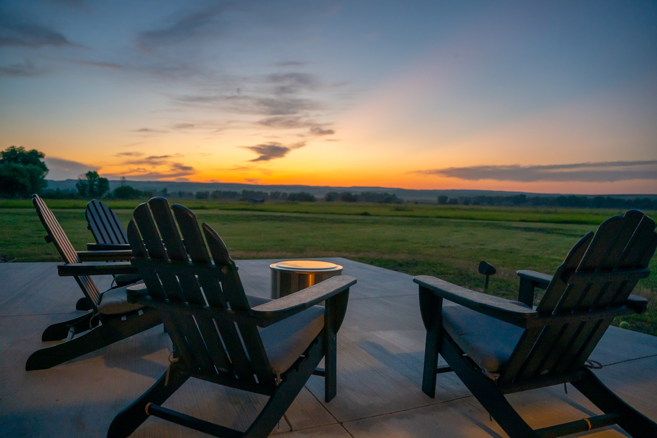 Adirondack chairs on the 3 Mile Cabin patio at sunset, overlooking Montana fields